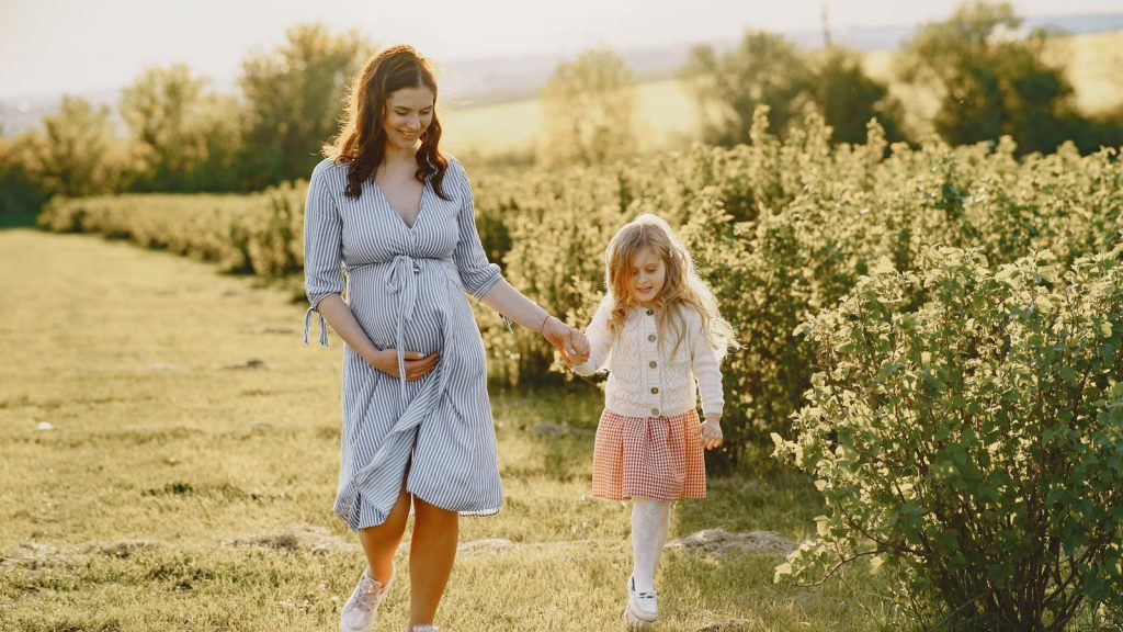 Expectant mother walking through a field holding her daughter's hand