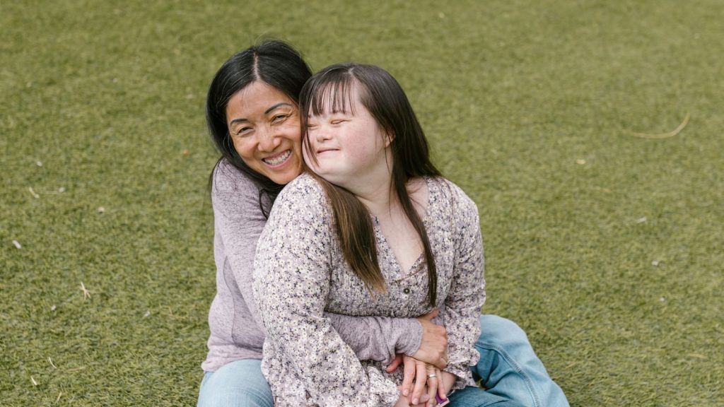 Mother sitting on the grass hugging her daughter